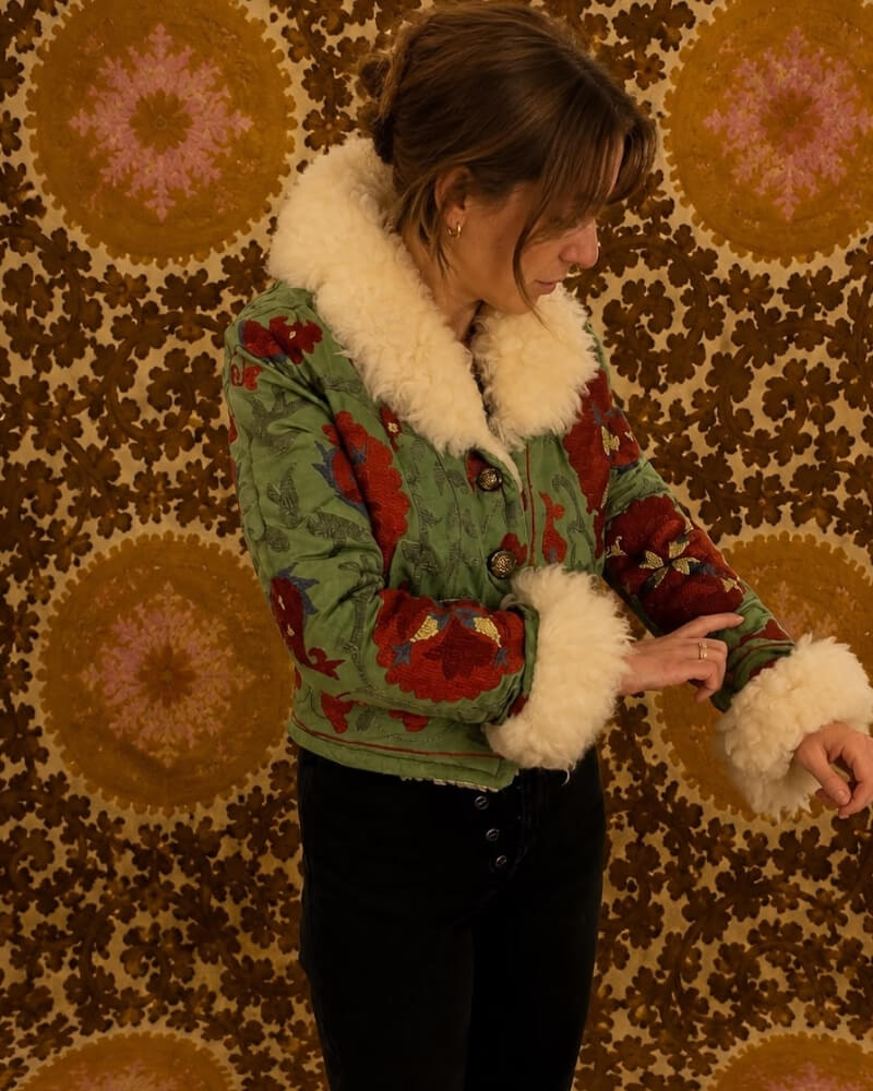 The Afghan Coat Coco No. 2 by Lunaré – detail shot on model, green coat with red floral embroidery and cream shaggy shearling collar and cuffs.