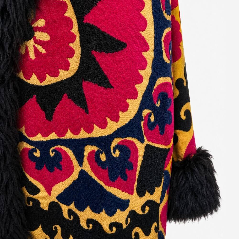 Close-up back detail of the Long Afghan Coat in yellow, showing bold red, navy and gold embroidered sun and heart motifs with a black shearling trim.