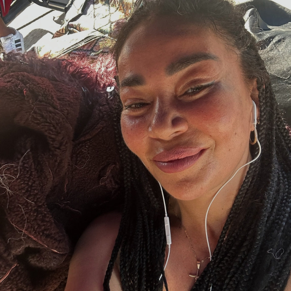 Close-up selfie of a woman with braided hair wearing earphones, resting outdoors, part of Lunaré's behind-the-scenes production photos.