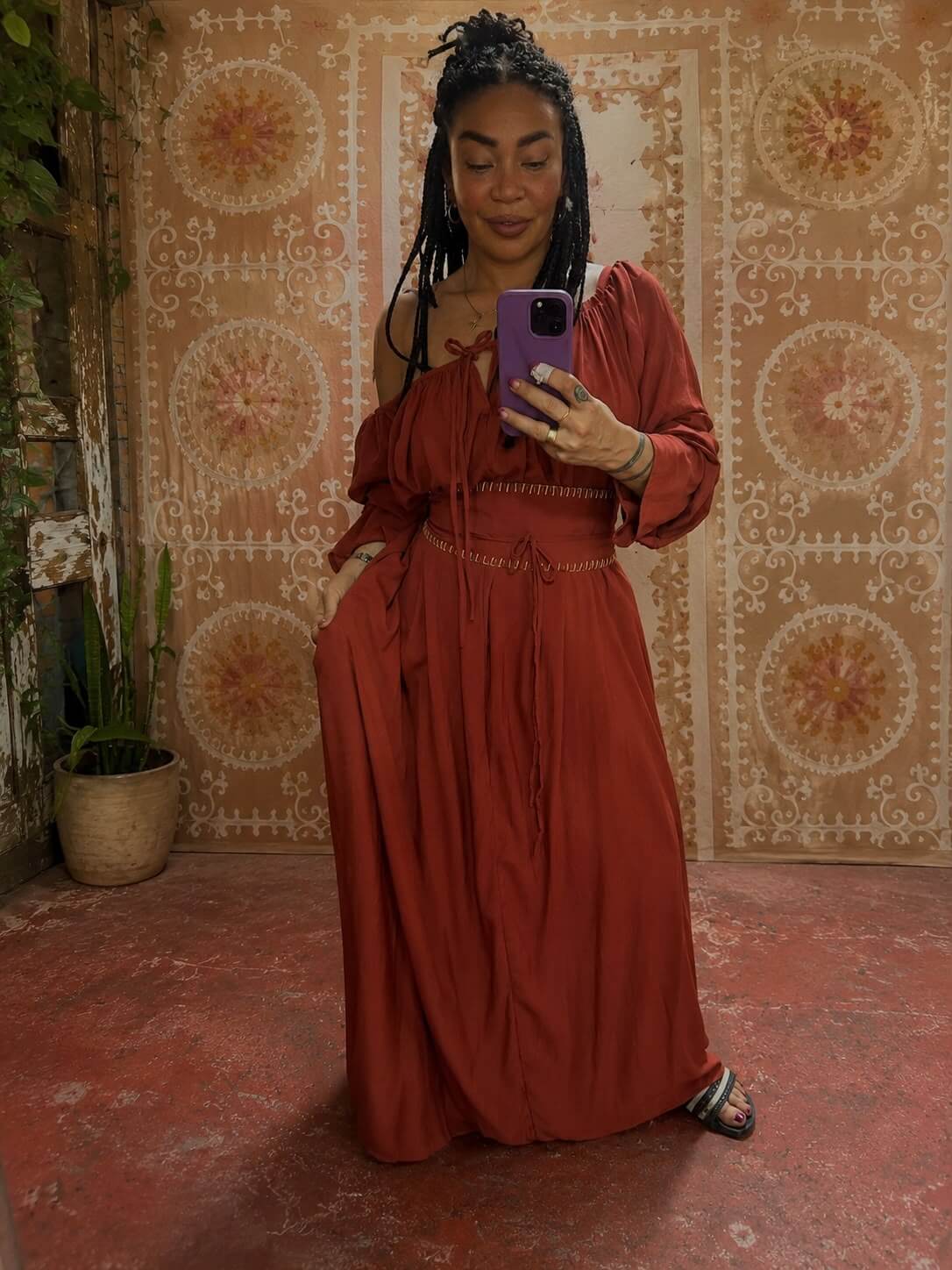Woman wearing the Sanaya Kim Dress in rust viscose, taking a mirror selfie against a patterned wall.