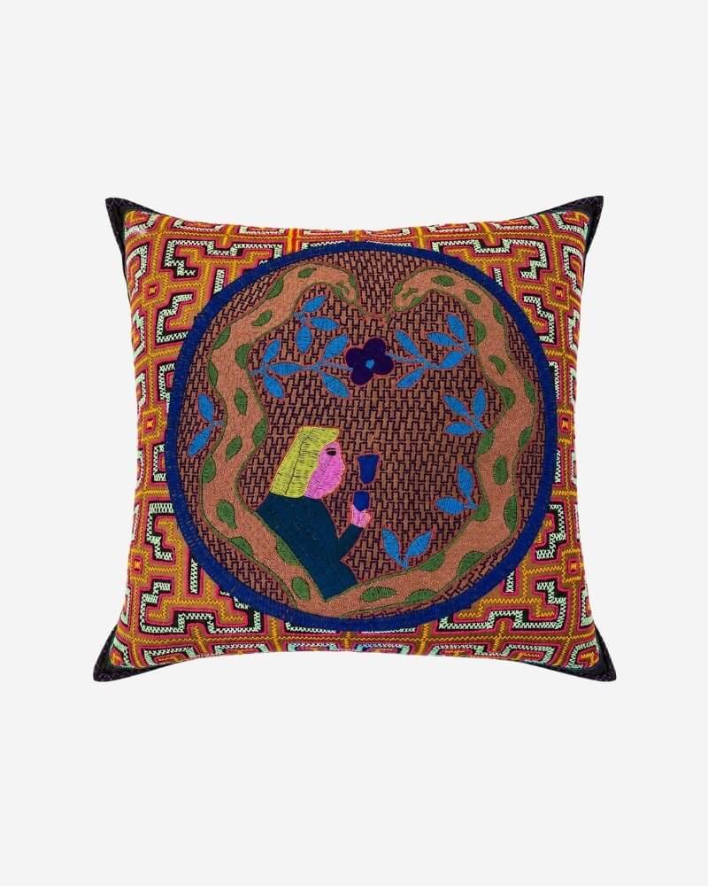 Hand-Embroidered Shipibo Cushion No. 6 in rust, with a bold zigzag geometric border and a central navy medallion depicting a stylised woman's profile surrounded by blue leaf branches and purple flowers.