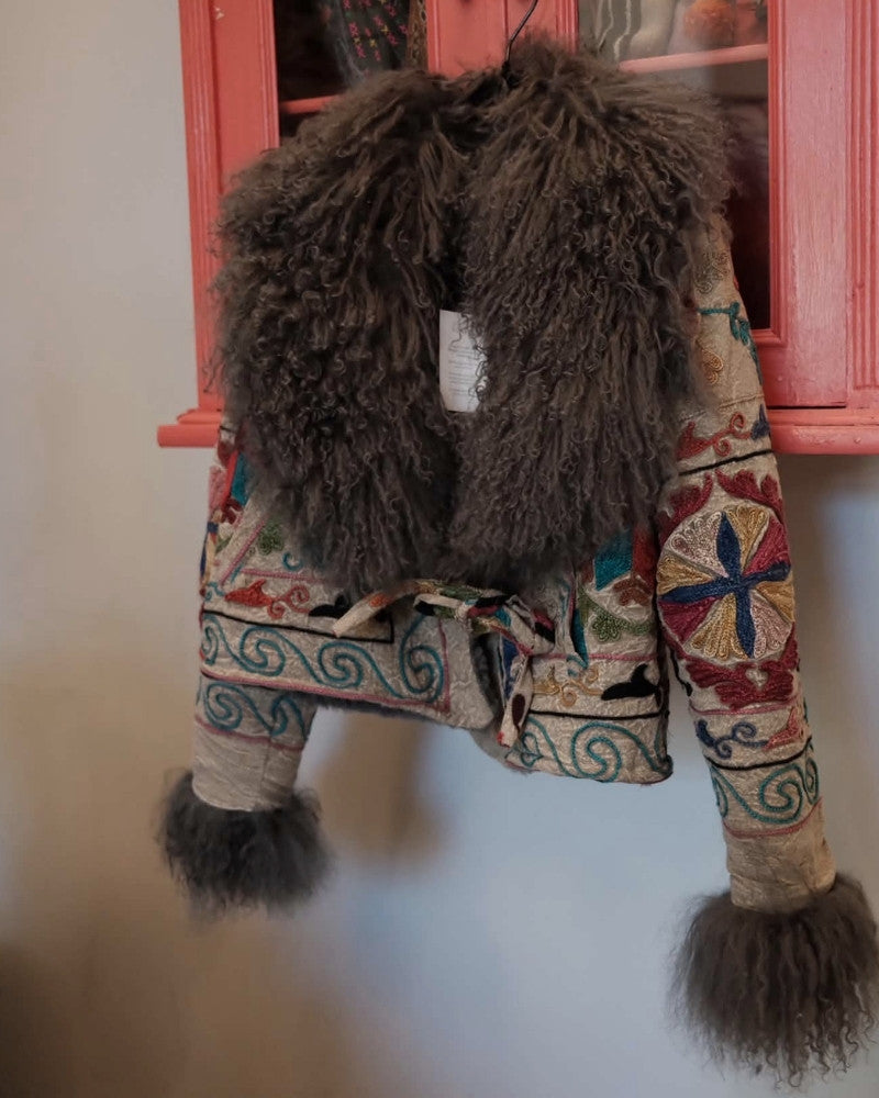 The Afghan Coat Martina No. 3 by Lunaré – detail shot, multicolor embroidered coat with brown shaggy shearling trim hanging against a rustic backdrop.