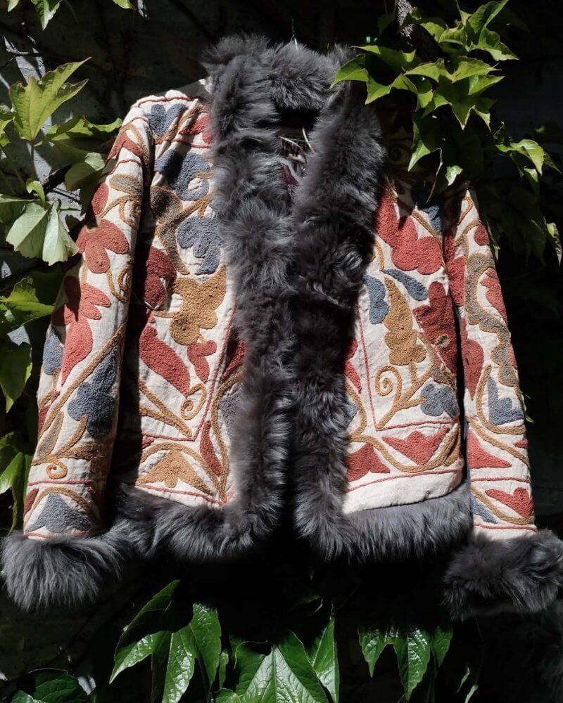 The Afghan Coat Eliza by Lunaré – flat lay outdoors, cream floral embroidered coat in rust, blue and gold with grey shaggy shearling collar and cuffs.