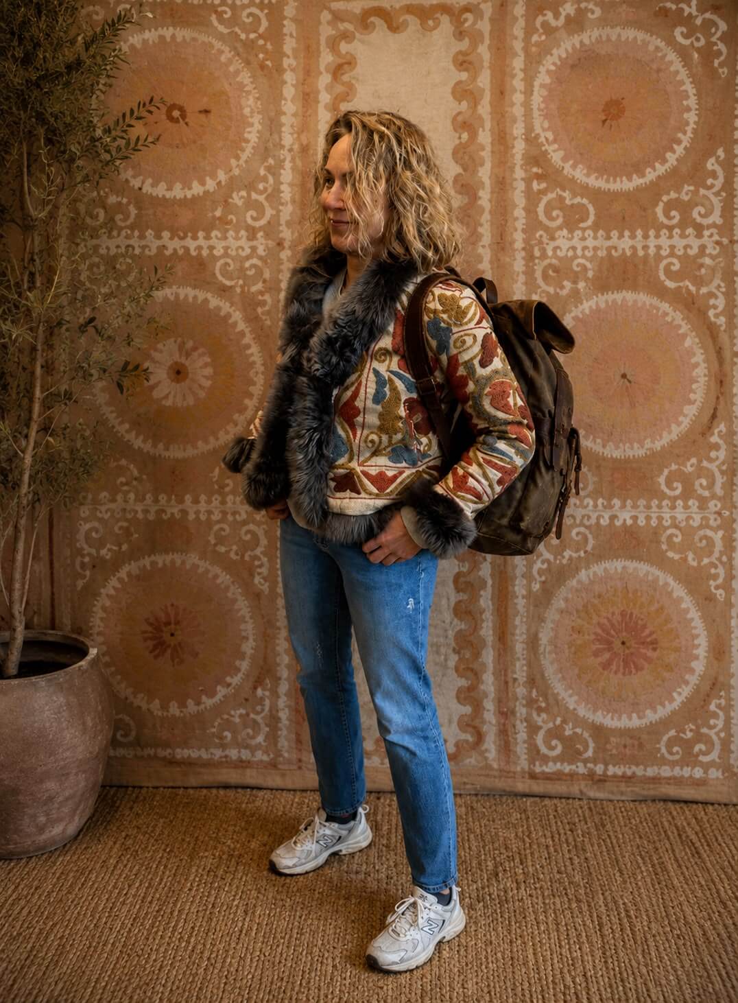The Afghan Coat Eliza by Lunaré – model wearing the hand-embroidered floral jacket with dark grey shaggy fur trim, styled with jeans.