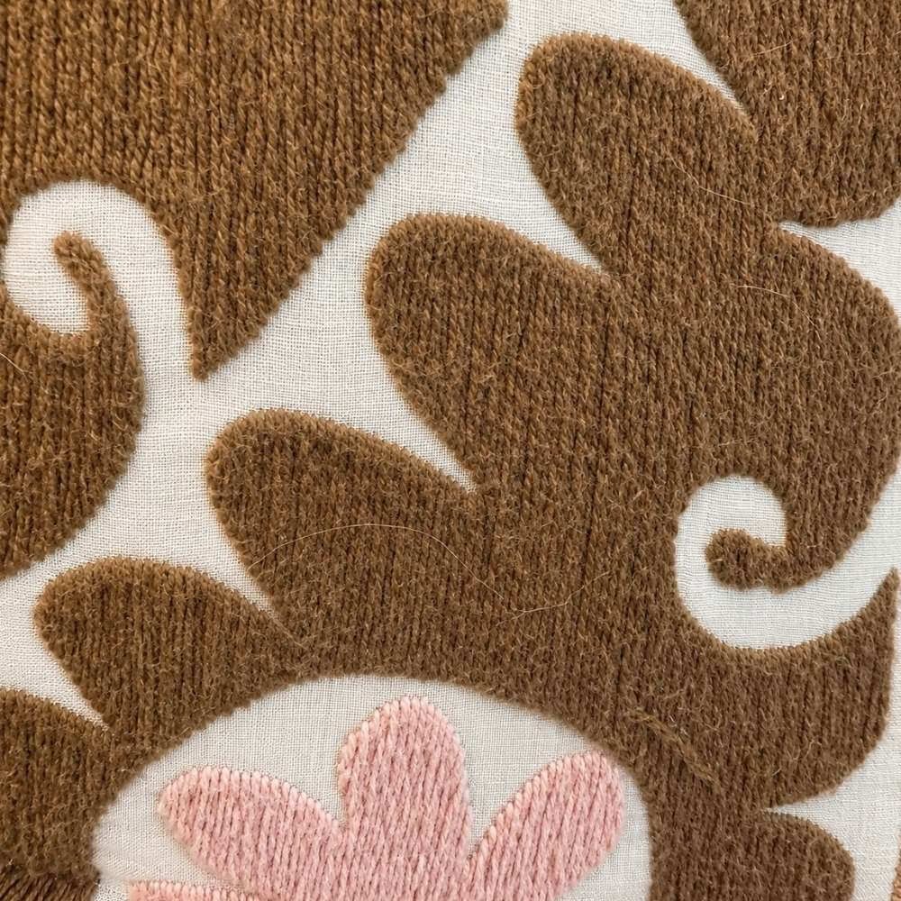 Close-up detail of the Martina Afghan Jacket No. 11 fabric, showing the hand-embroidered swirl pattern in mustard brown and cream with a pink floral accent.