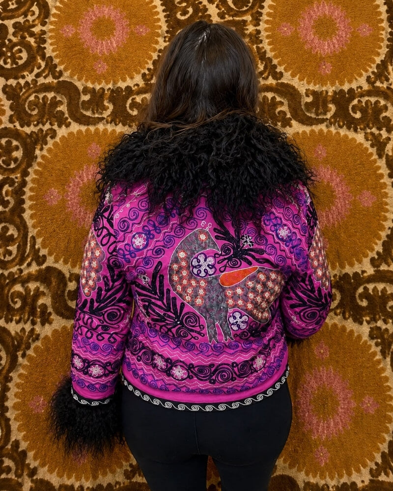 The Afghan Coat Martina No. 2 by Lunaré – back view on model, hand-embroidered stylized animal motif in orange, cream and grey on a bright pink base, black shaggy shearling collar and cuffs.