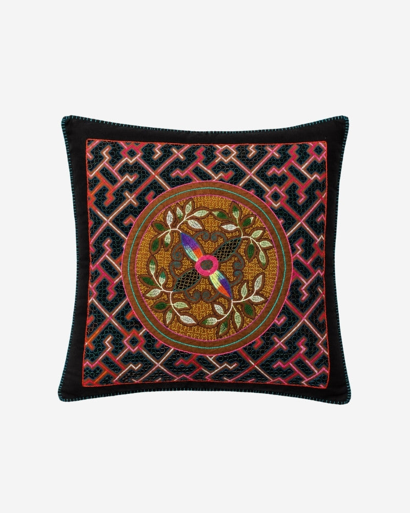 Hand-Embroidered Shipibo Cushion No. 10 in dark teal, with a pink geometric maze border and a central medallion featuring a rainbow-coloured bird motif encircled by leaves.