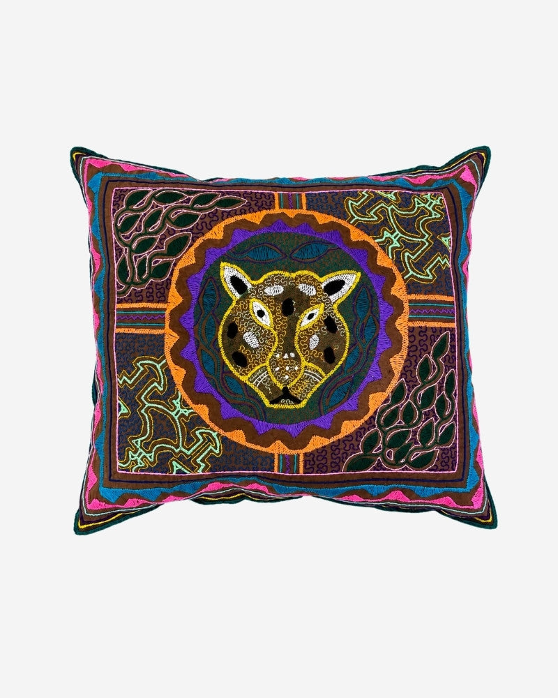 Hand-Embroidered Shipibo Cushion No. 16 in dark purple, with a central jaguar face motif surrounded by concentric circles and green leaf embroidery in the corners.