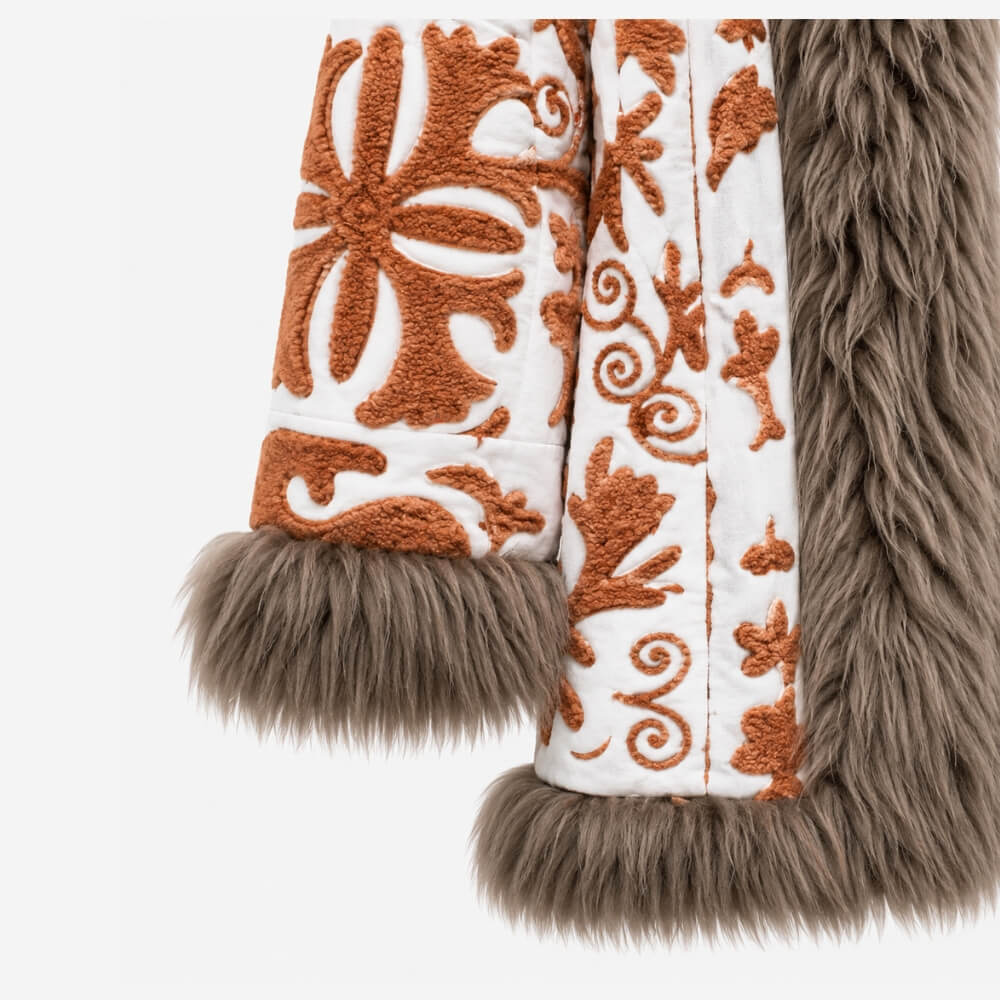 The Afghan Coat Jasmia No. 1 by Lunaré – close-up detail of the rust hand-embroidered floral pattern on cream fabric with taupe shaggy shearling cuffs and front trim.