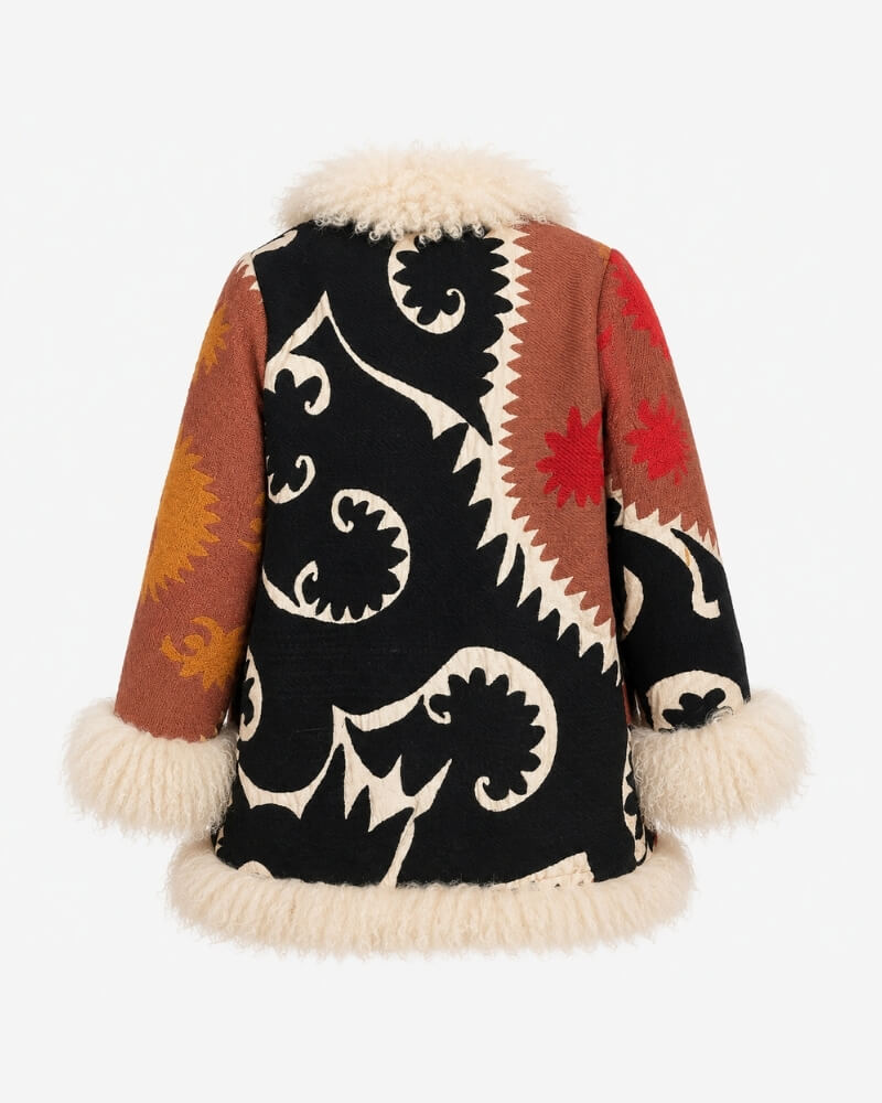 The Afghan Coat Jasmia No. 2 by Lunaré – back view, black embroidered swirl pattern panel with rust and orange geometric patchwork sleeves and cream shaggy shearling trim.