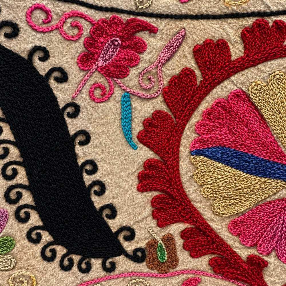 Close-up detail of The Martina Coat No. 9 embroidery, showing the hand-stitched red, pink and gold floral scrollwork with black paisley outlines on tan fabric.