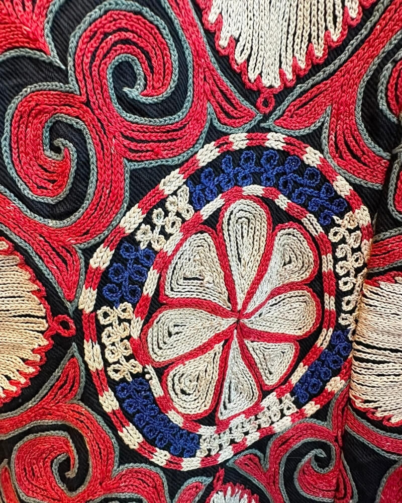 The Afghan Coat Ragna No. 4 by Lunaré – close-up embroidery detail on matching bag, hand-embroidered floral medallion in red, cream and navy on black.
