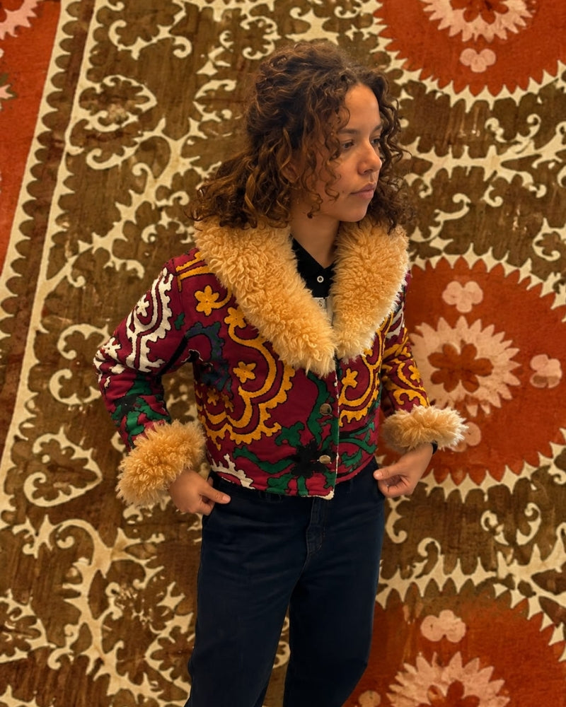 The Afghan Coat Coco No. 3 by Lunaré – lifestyle shot on model, burgundy and green paisley patterned coat with tan shaggy shearling collar and cuffs.