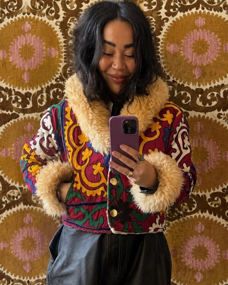 The Afghan Coat Coco No. 3 by Lunaré – lifestyle mirror shot on model, burgundy and green paisley patterned coat with cream shaggy shearling collar and cuffs.