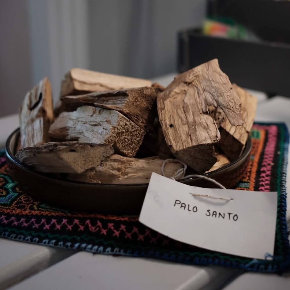Palo Santo by Lunaré – lifestyle shot, raw wood sticks in a bowl on a woven textile pouch with handwritten label.